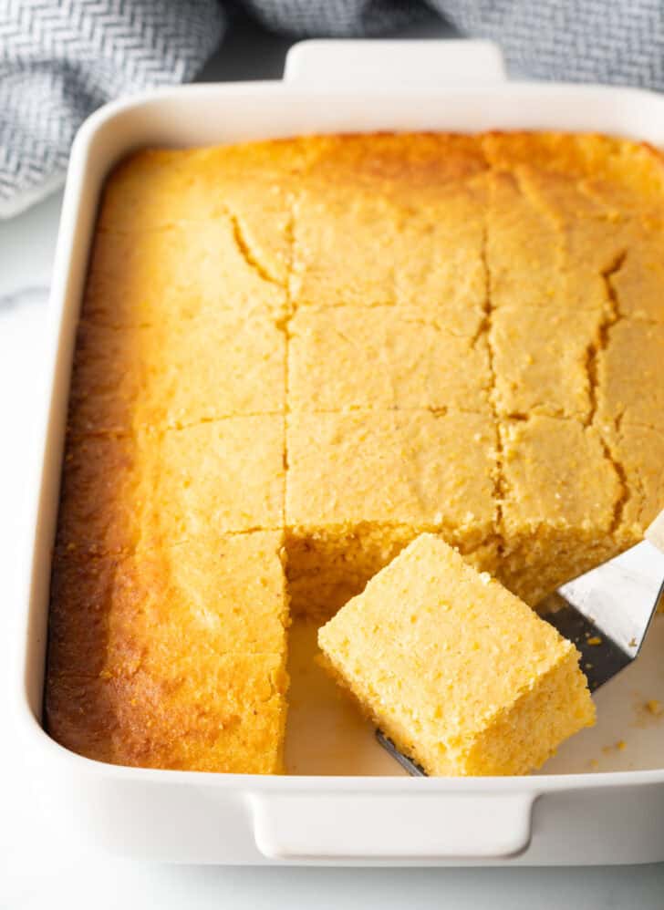 Top down view rectangle baking dish of cornbread, cut into even squares. A metal spatula is removing a square of cornbread from the pan.