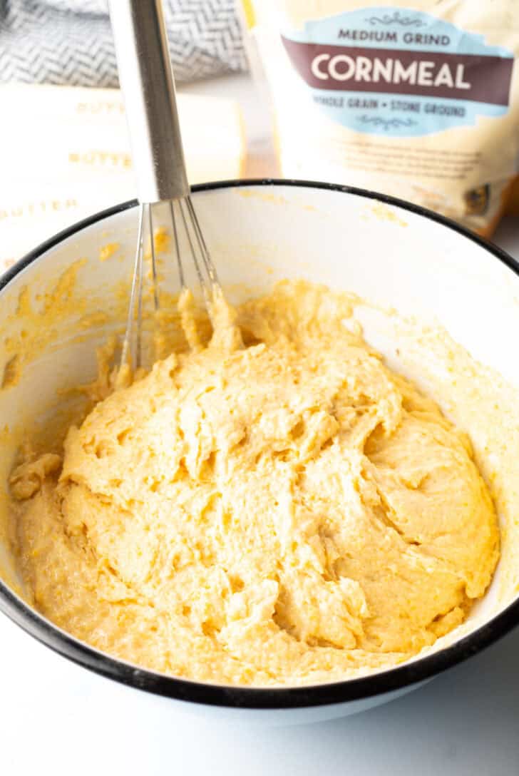 Cornbread batter in a white mixing bowl with a whisk.