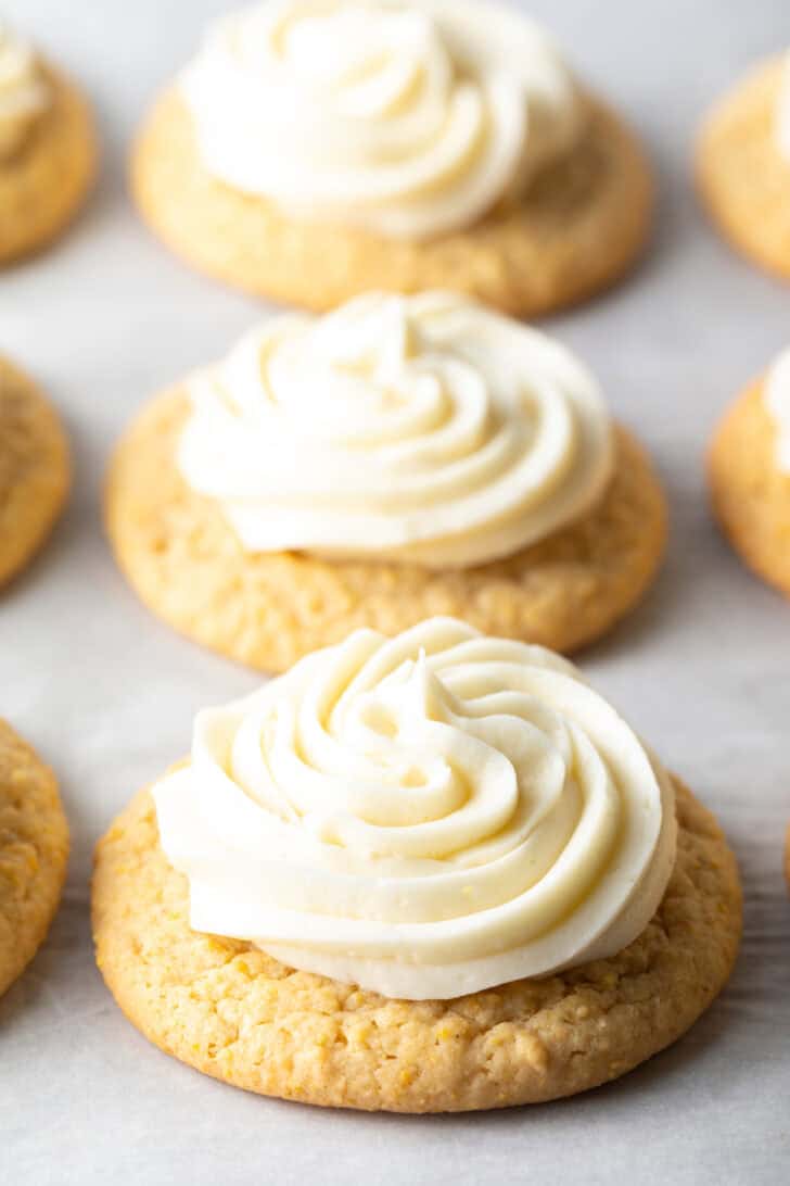 Several honey butter cornbread cookies on a white background, each topped with piped frosting.