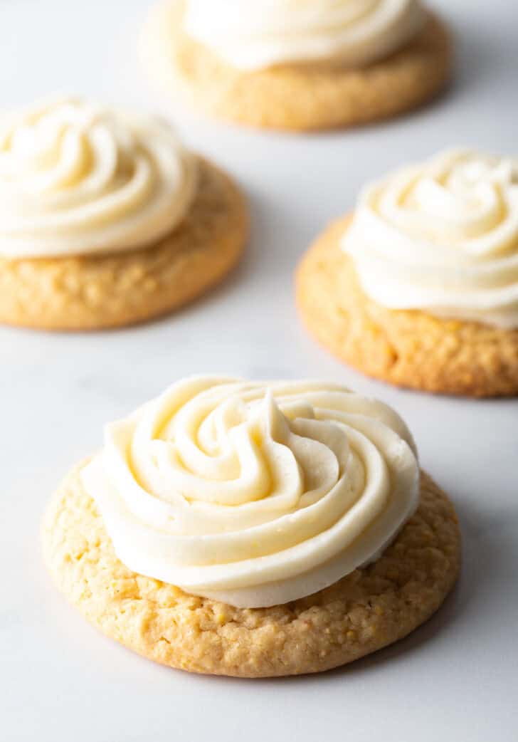 Several honey butter cornbread cookies on a white background, each topped with piped frosting.