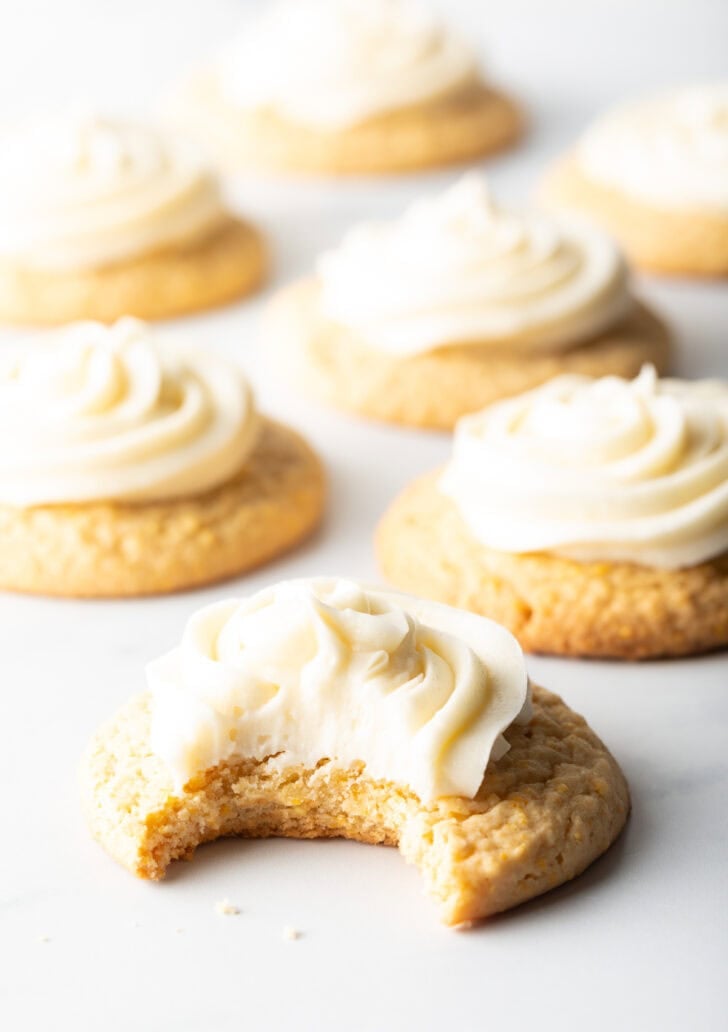 Several honey butter cornbread cookies on a white background, each topped with piped frosting. The cookie closest to camera has a bite taken out.