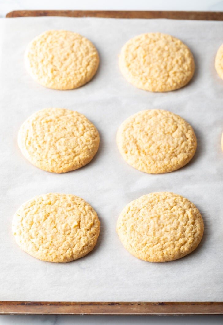 6 flat baked cornbread cookies on a baking sheet.