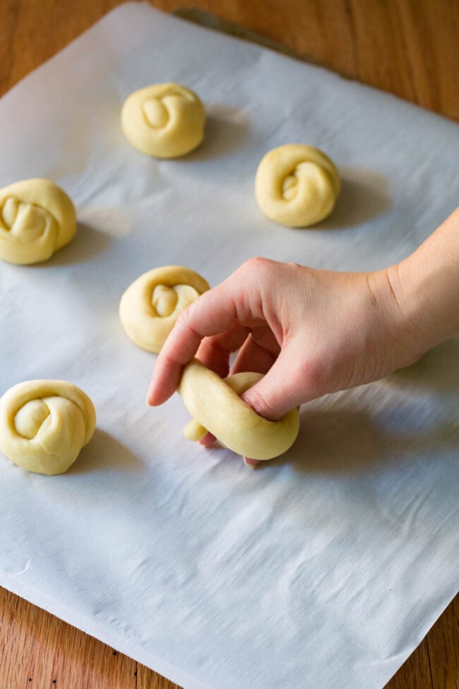 Hand holding yeast dough and tying it in a knot. 