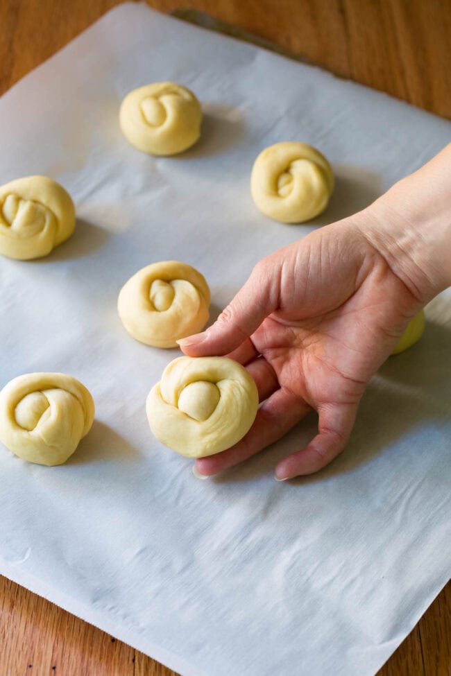 Hand holding a yeast dough roll tied in a knot and placed on a baking sheet. 