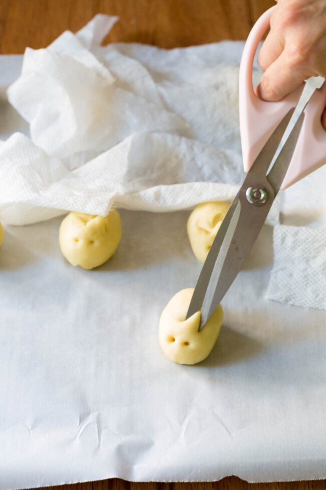 Hand holding scissors to make bunny ears in the yeasted dough. 