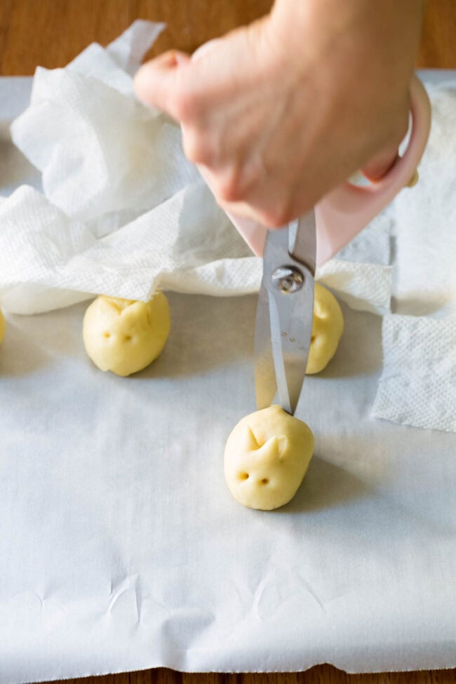 Hand holding scissors to cut a small slit in the dough to make a bunny tail. 