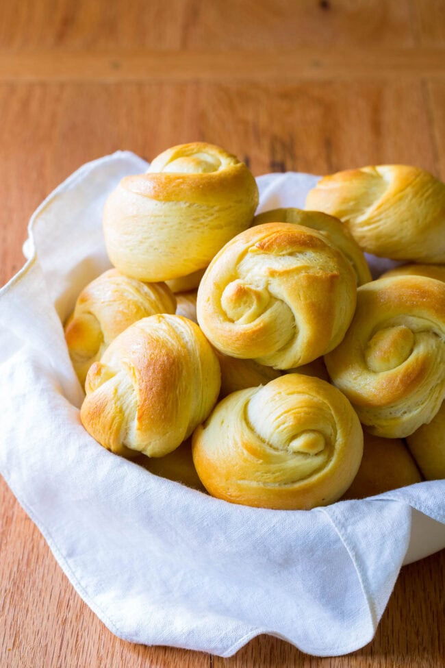 Yeast dinner rolls in a serving basked lined with a white linen. 