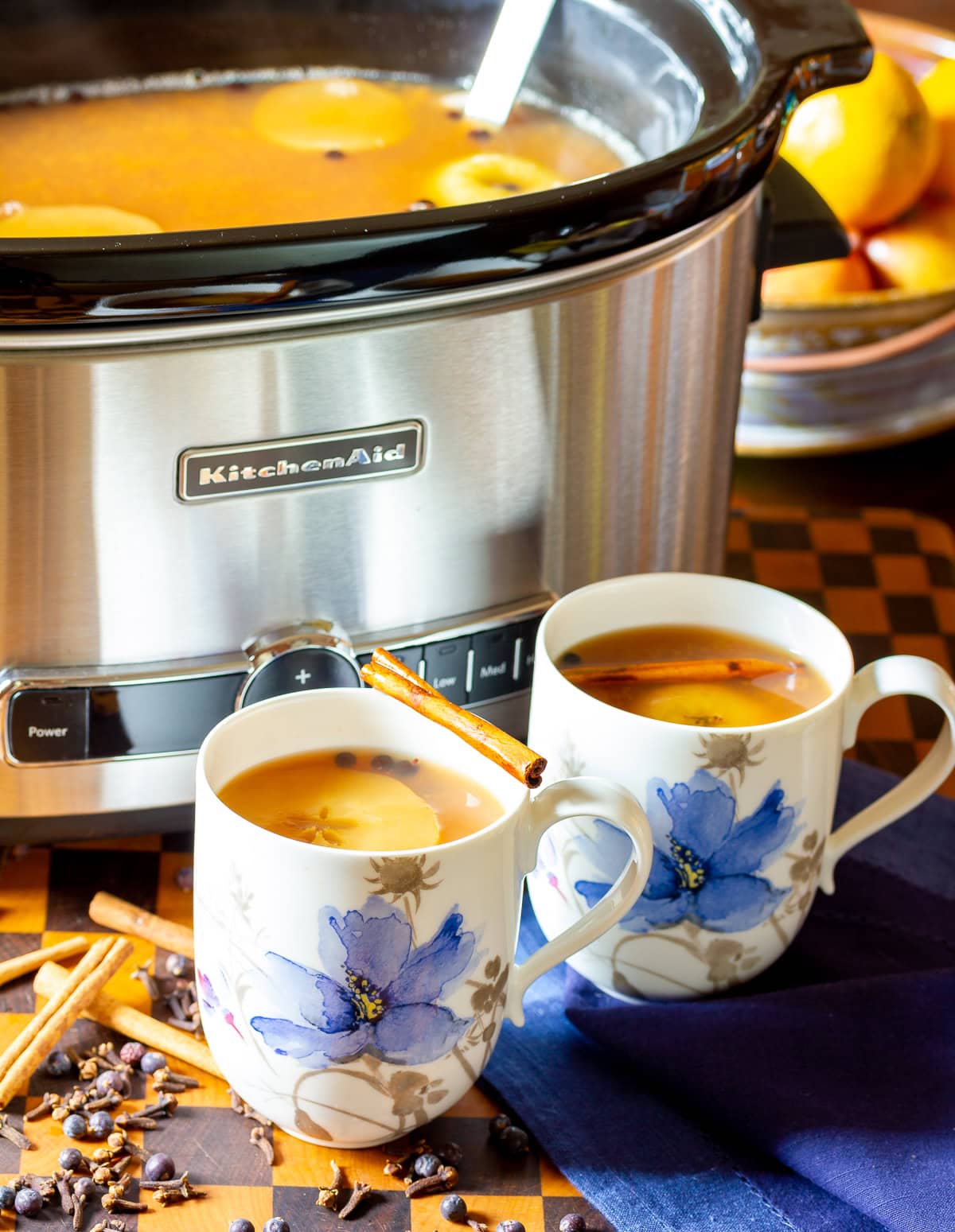 Two mugs with apple cider wassail in them with the crockpot full of more cider in the background. 