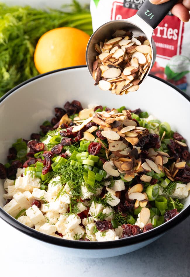 Adding sliced almonds and dried cherries to the white mixing bowl.