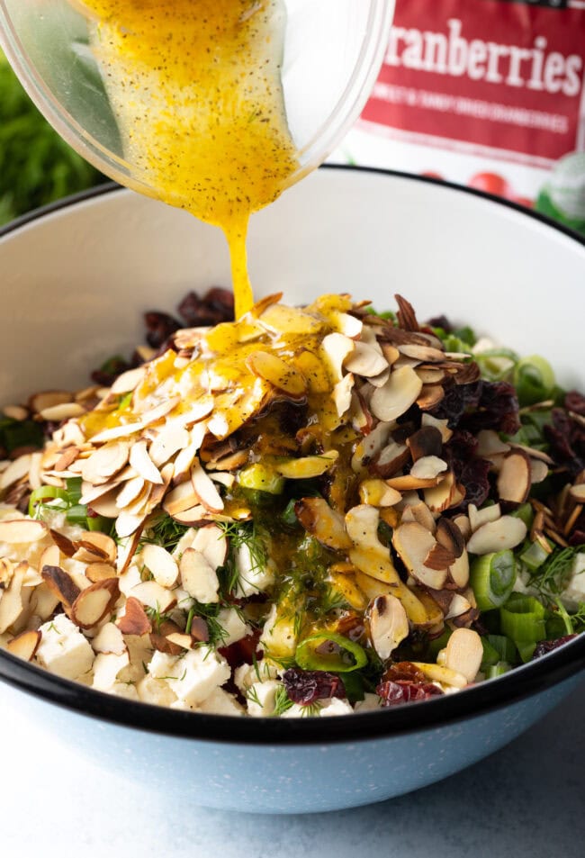 Pouring lemon vinaigrette over the salad in a white bowl.