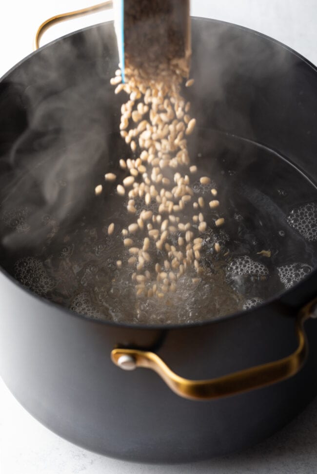 Pouring grains into black pot of water.