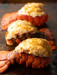 Three plump cooked lobster tails on a baking sheet.
