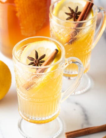 2 glass handled mugs with hot toddy, garnished with star anise and a cinnamon stick.