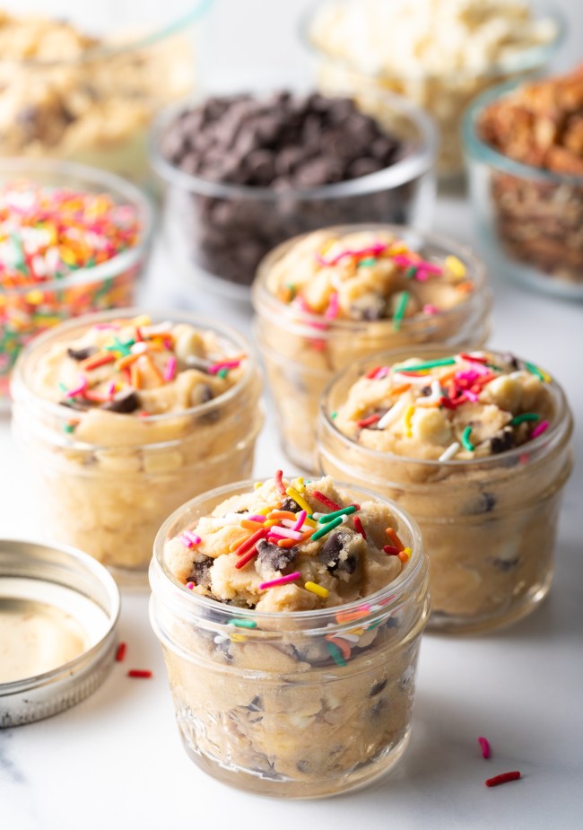 Four small glass containers with edible cookie dough topped with sprinkles.