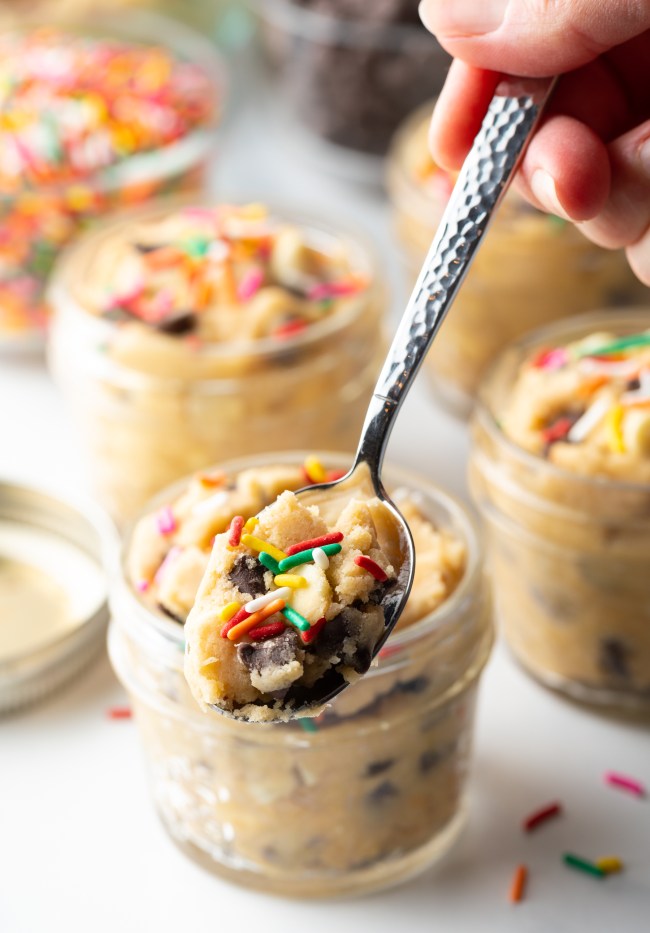 Metal spoon with cookie dough and sprinkles, held to camera.