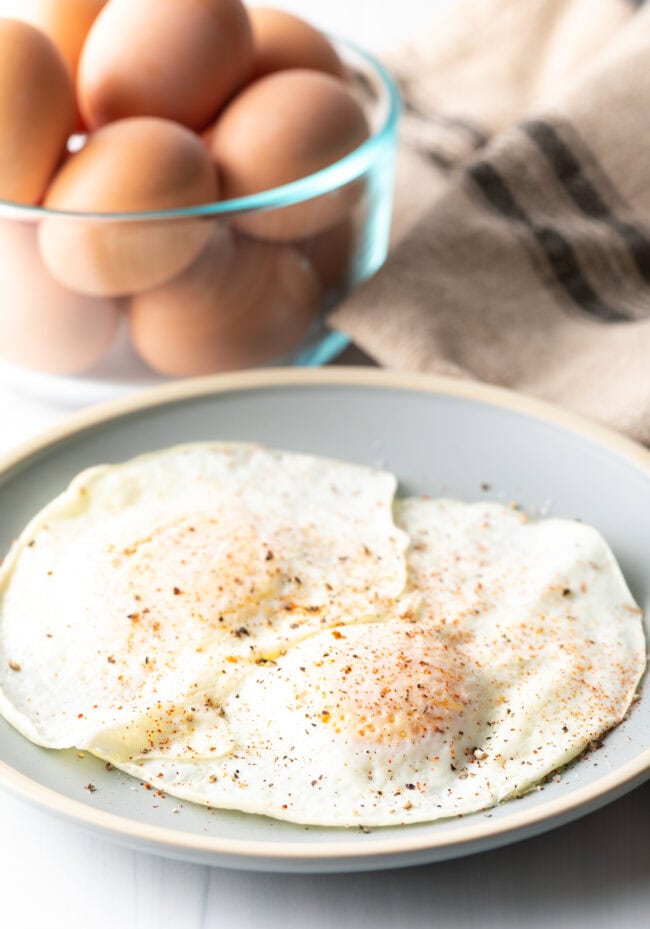 Two cooked eggs over easy on a light blue plate, sprinkled with spices.