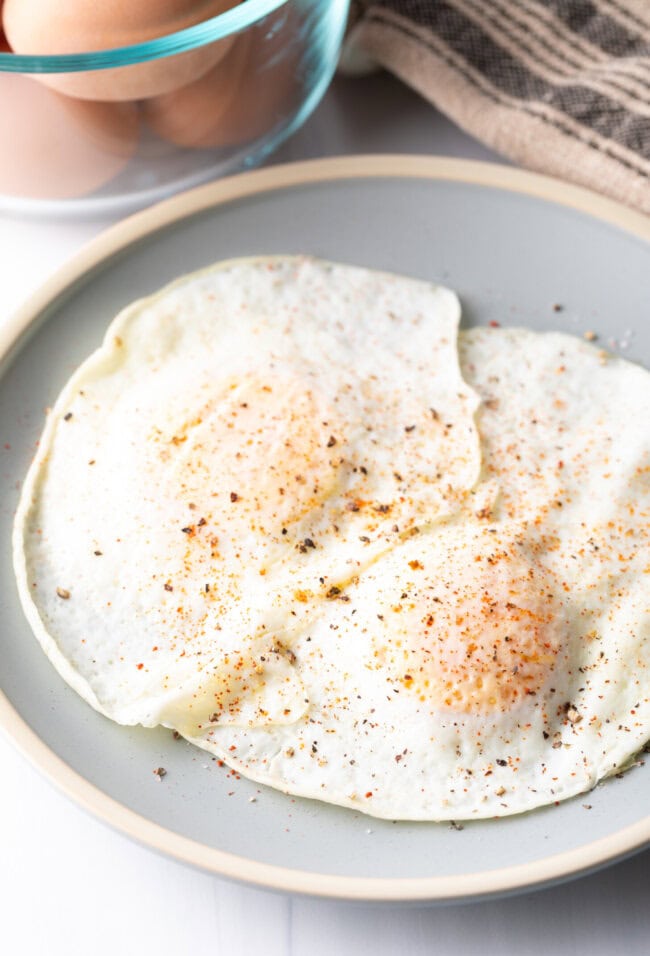 Two cooked eggs over easy on a light blue plate, sprinkled with spices.