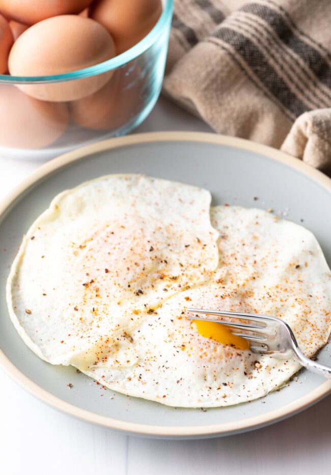 Fork cutting into th soft yolk of a gently over easy fried egg, on a light blue plate.