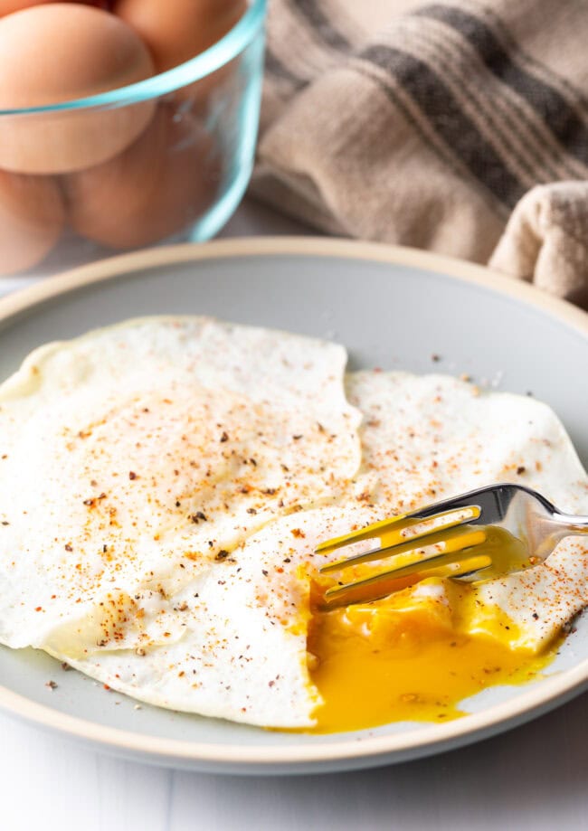 Fork cutting into th soft yolk of a gently over easy fried egg, on a light blue plate.