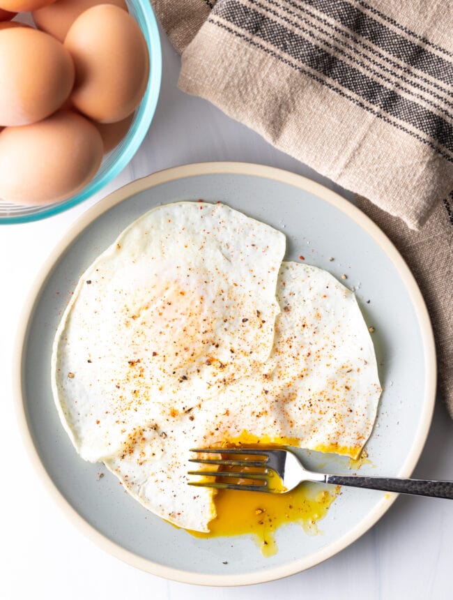 Fork cutting into th soft yolk of a gently over easy fried egg, on a light blue plate.