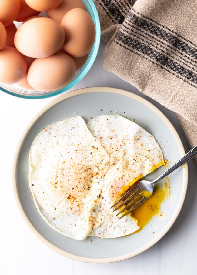 Fork cutting into th soft yolk of a gently over easy fried egg, on a light blue plate.