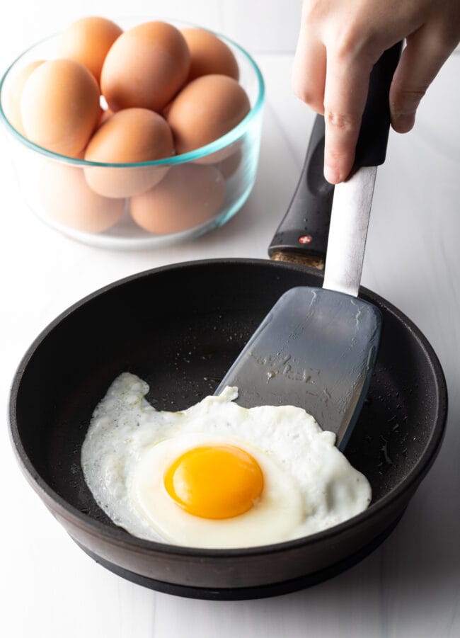 Flipping a fried egg with a black spatula over a black skillet.