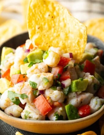 Yellow bowl of shrimp ceviche with a tortilla chip sticking in the middle.