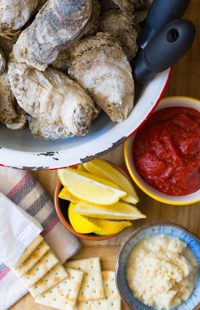 Oysters in a pot next to lemons, cocktail sauce, horseradish and saltines. 