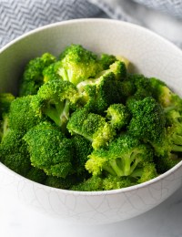 Bright green steamed broccoli in a white bowl.