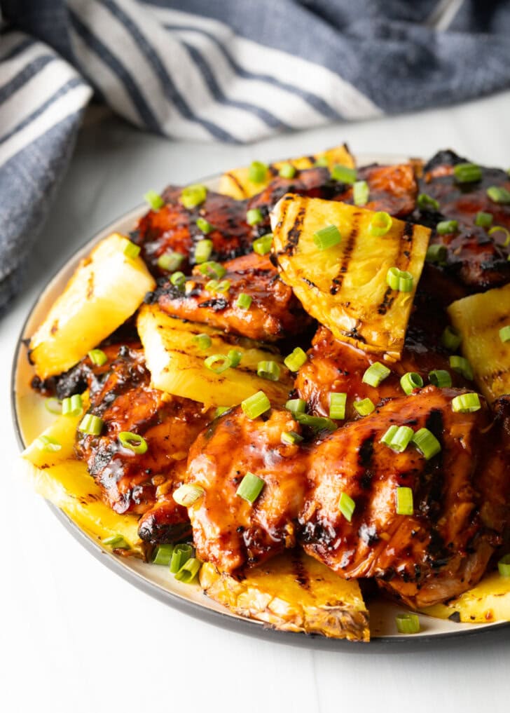 Sticky huli huli chicken pieces topped with chopped scallions and grilled slices of pineapple.