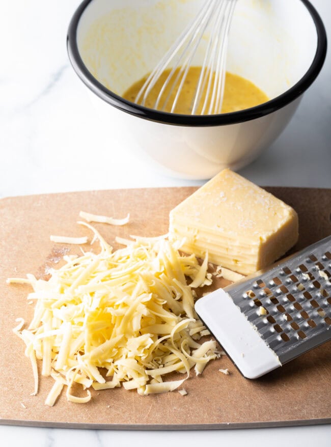 Shredded cheddar cheese on a cutting board.