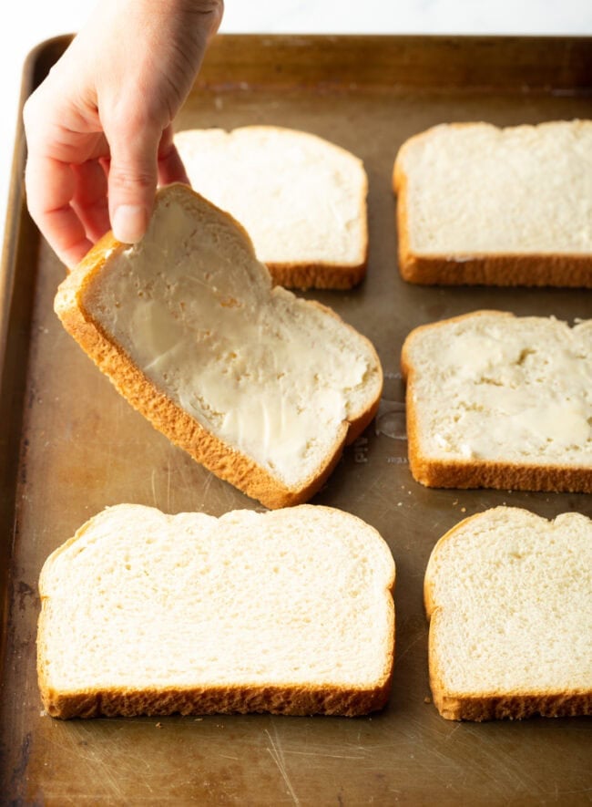 Hand placing piece of buttered bread on a baking sheet.