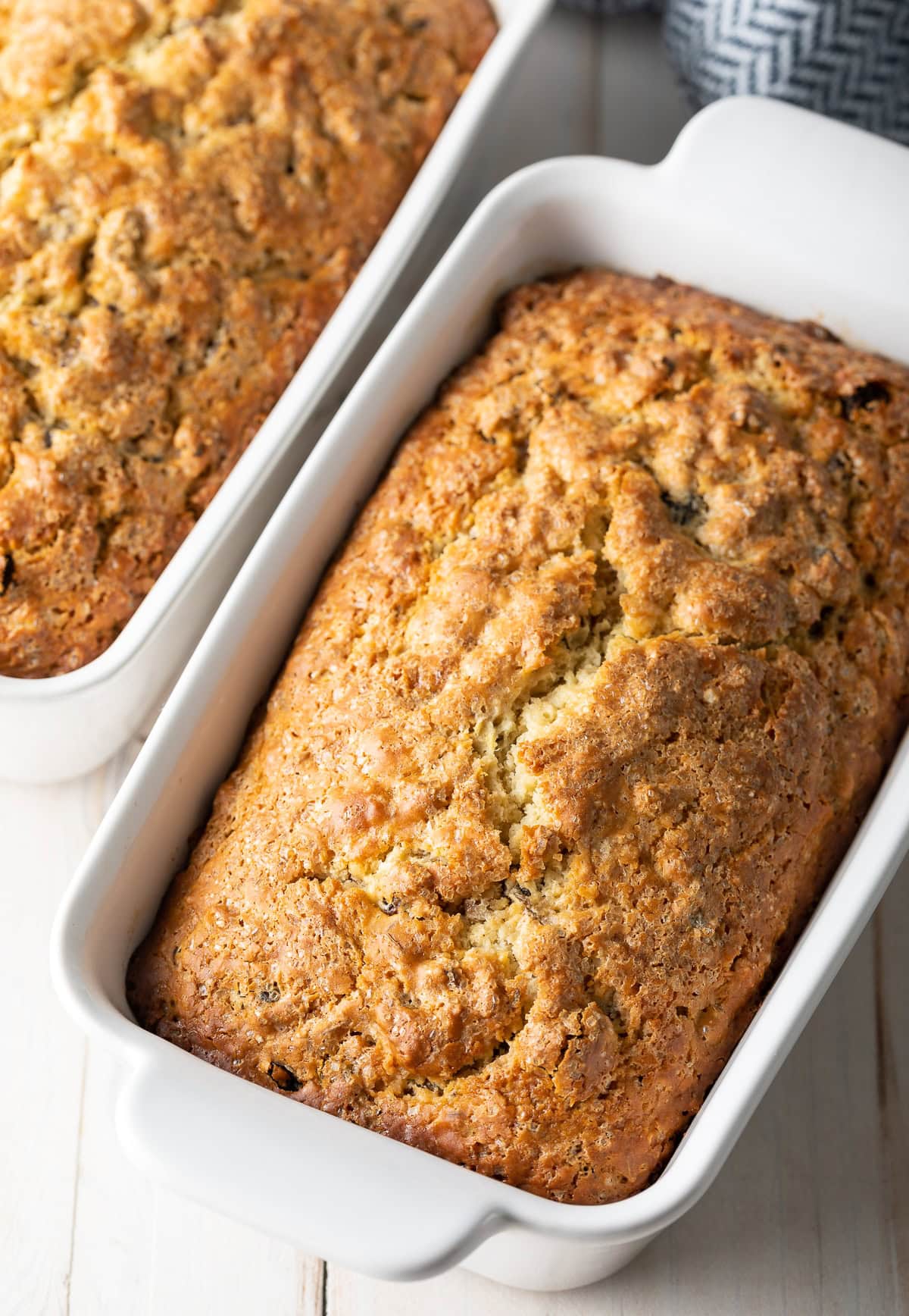 Two loaves of raisin Irish soda bread baked in white ceramic loaf pans. 