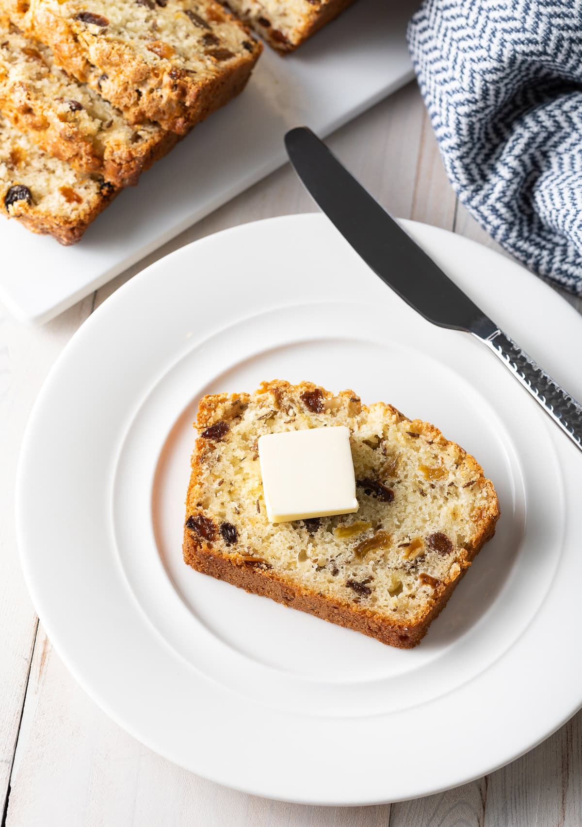 Slice of this Irish soda bread with raisins on a plate with butter on top. 