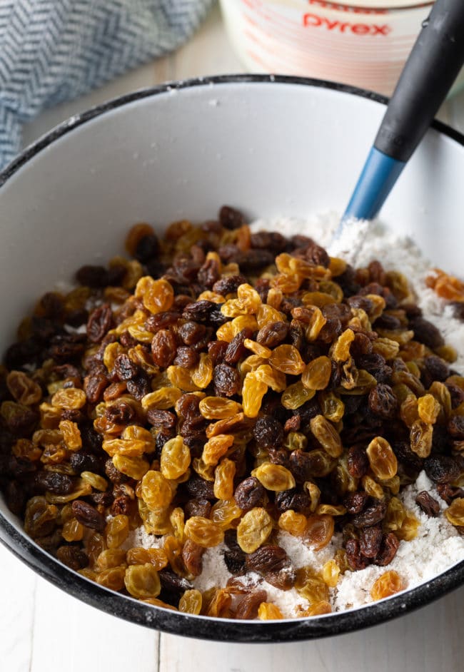 Raisins mixed with flour in a white mixing bowl. 