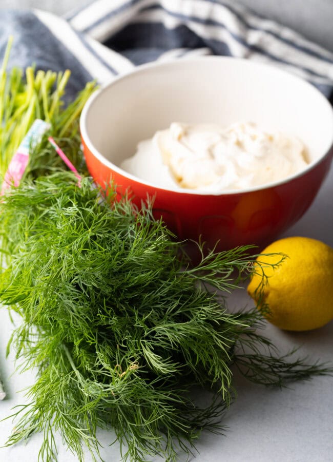 Recipe ingredients: Fresh herbs, whole lemon, bowl of sour cream.