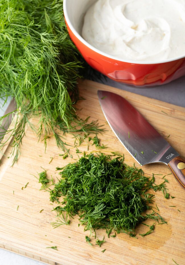 Fresh dill chopped on a wood cutting board with large knife.