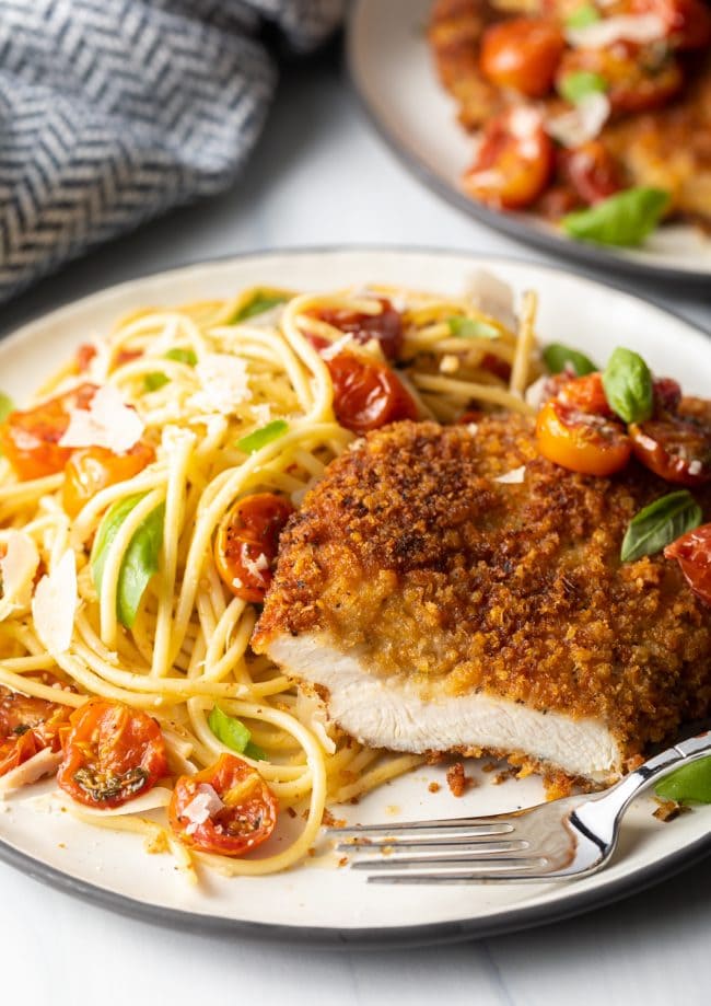 final shot showing Italian chicken cutlet cut into with a fork on a plate, spaghetti and cherry tomato sauce on the side