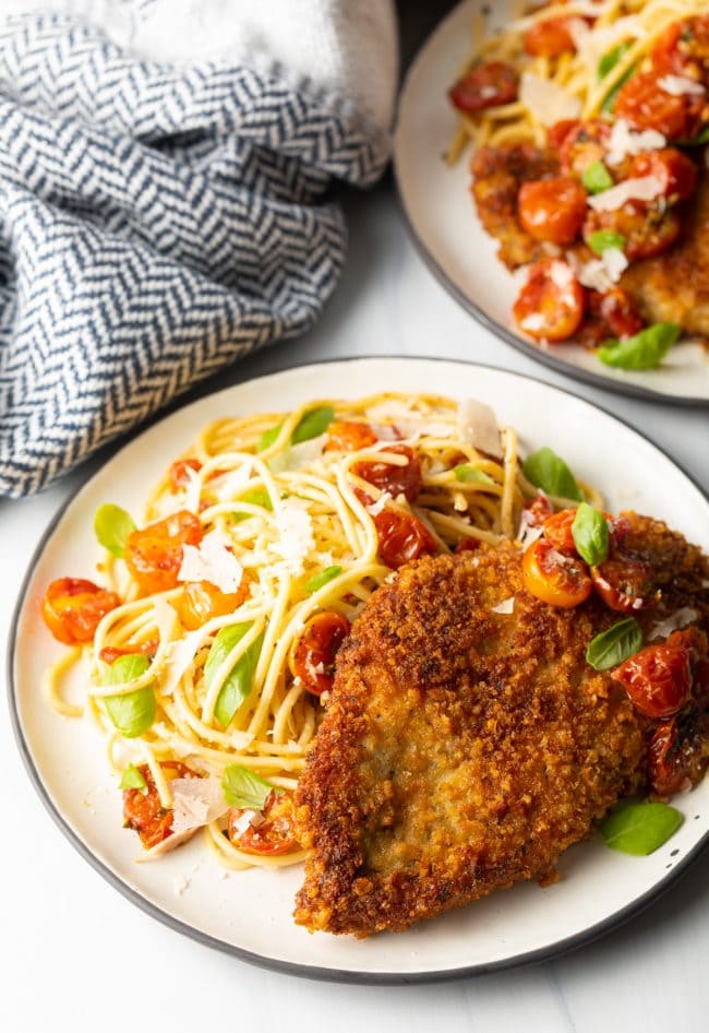 finished plate of pan fried or oven baked crispy Italian chicken cutlets with pasta and cherry tomato sauce on the side