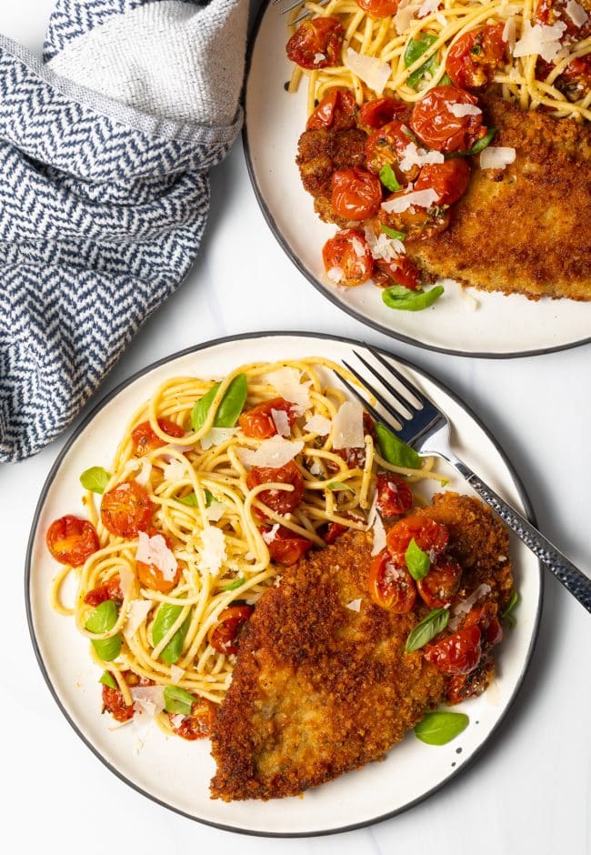 overhead view two plates of pasta with fried chicken breasts and cherry tomato sauce