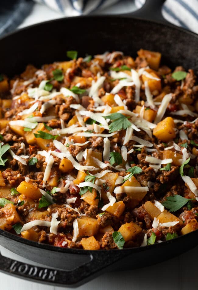 Ground beef and potatoes, topped with shredded parmesan cheese in a skillet.