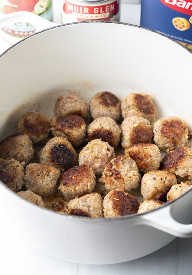 Seared meatballs in a large white soup pot.