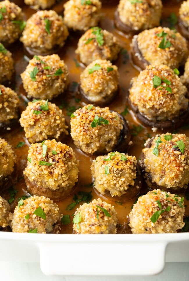 Two dozen baked Italian sausage stuffed mushrooms in a white baking dish.