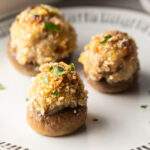 Three mushrooms stuffed with Italian sausage and cheese on a white plate.