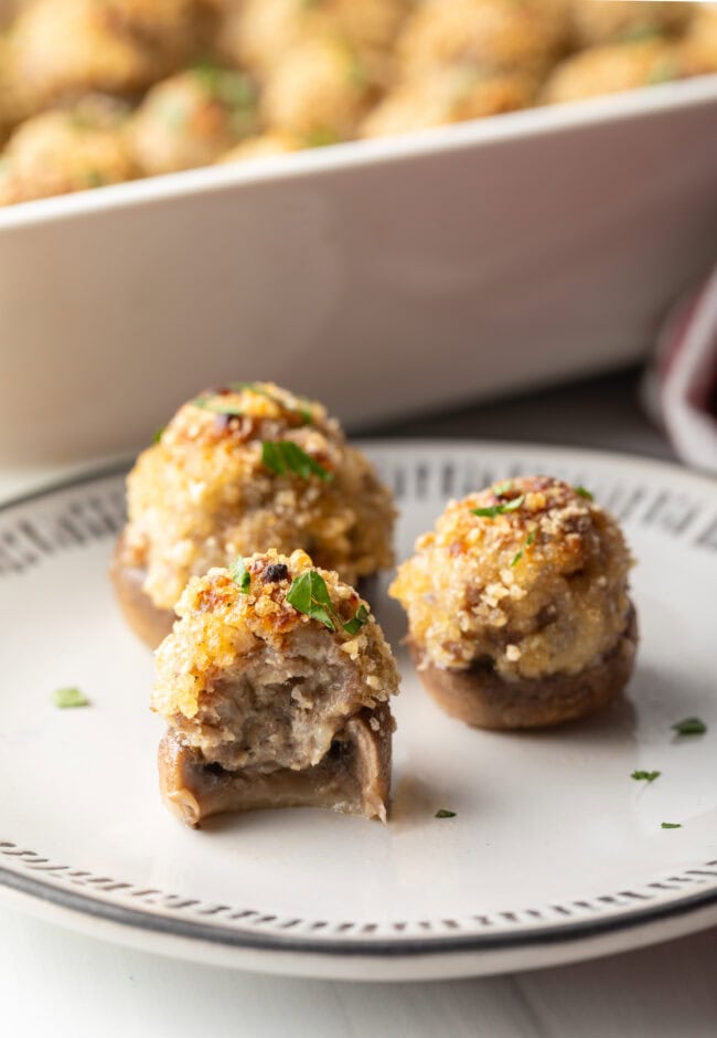 Three mushrooms stuffed with Italian sausage and cheese on a white plate. Front mushroom has been bitten in half to show inside.