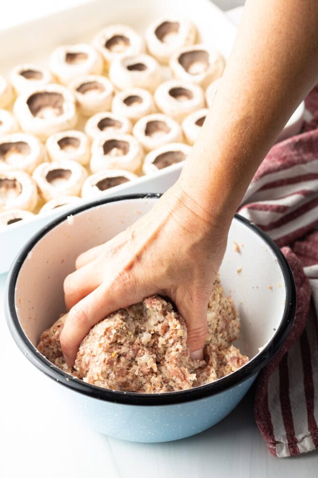 Hand mixing Italian sausage and cream cheese in a white mixing bowl.