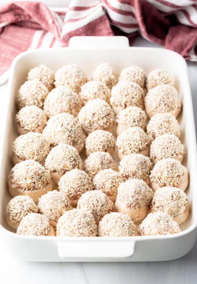 Approximately two dozen stuffed mushrooms unbaked in a large white baking dish.