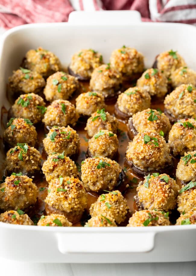 Two dozen baked Italian sausage stuffed mushrooms in a white baking dish.