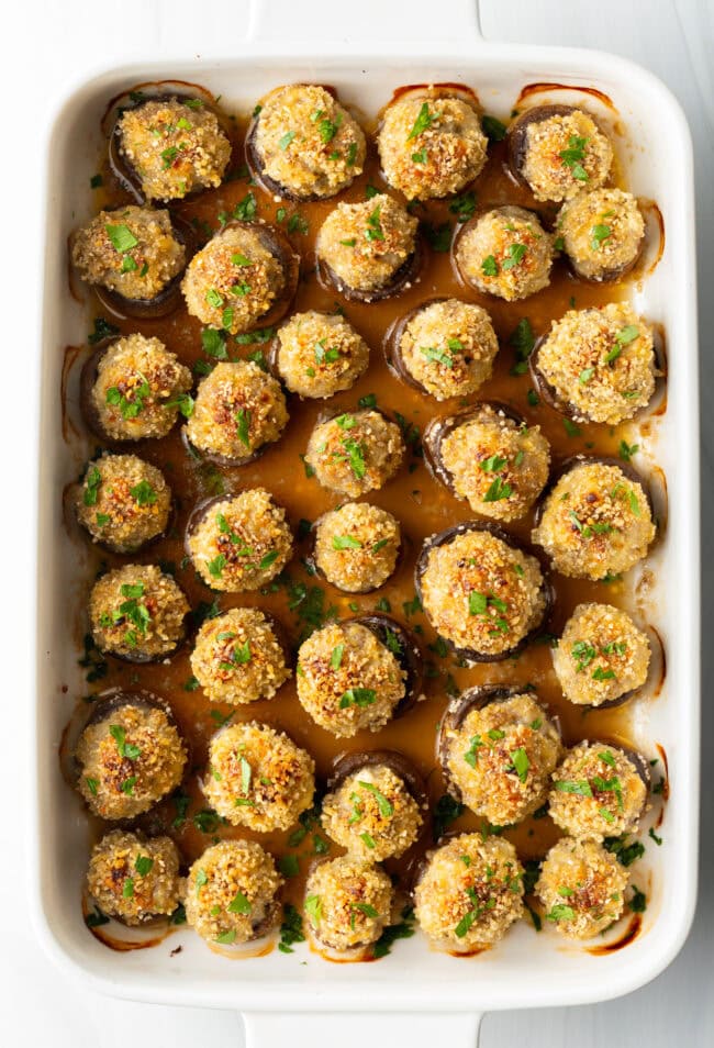 Top down view two dozen baked Italian sausage stuffed mushrooms in a white baking dish.