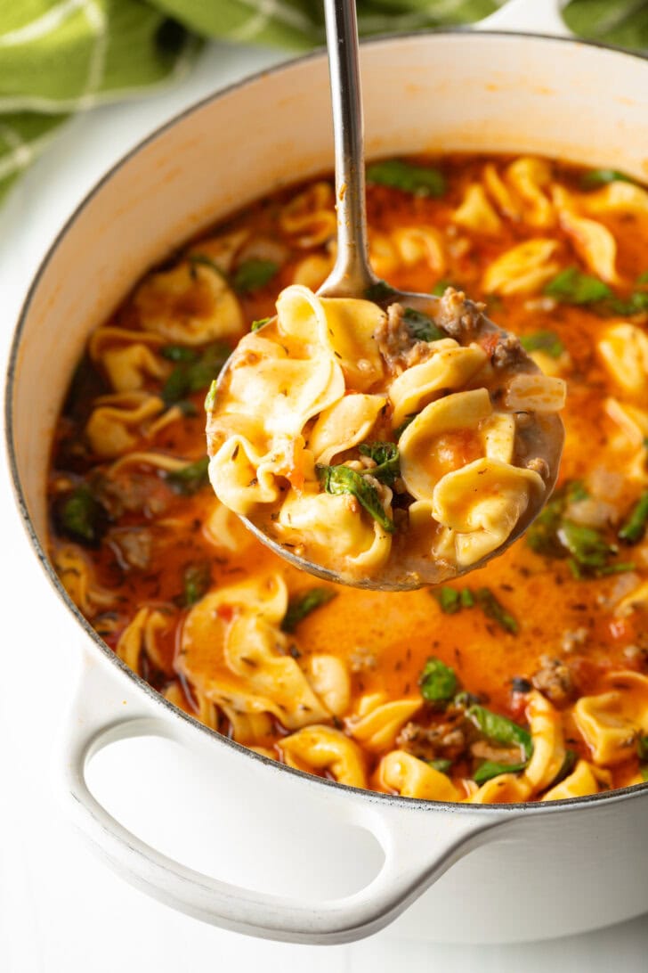 Metal ladle showing a scoop of tortellini soup to camera.